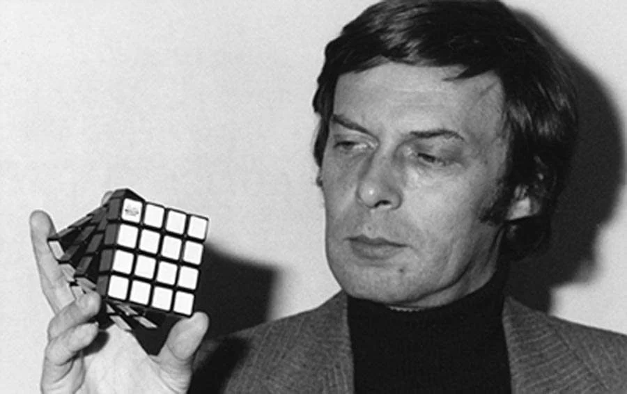 Ernõ Rubik, criador do cubo mágico, objeto usado como homenagem no Dia do Professor, segurando um cubo mágico