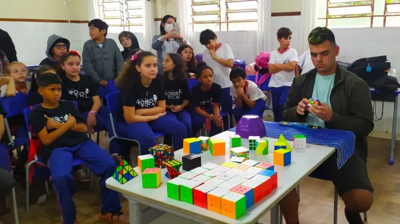 Imagem de um cubista mostrando diferentes modelos de cubo mágico em uma escola