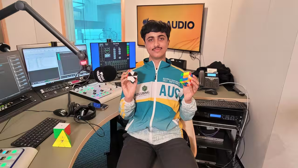 Imagem do competidor Divnoor Singh Bajwa segurando um cubo mágico em cada mão no SBS Studios, em Melbourne